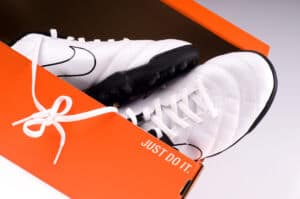 A new black and white pair, of a Nike indoor soccer shoes in orange packaging, with their traditional slogan.