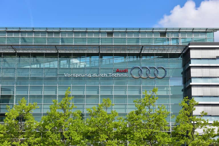 A glass building of the headquarters of the Audi factory with blue sky and trees in the foreground in Ingolstadt, Bavaria