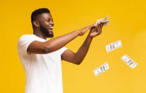 Happy african american man throwing out money banknotes, yellow studio background